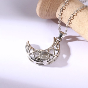 Detail of silver crescent moon pendant with geometric cutout and center stone on wood