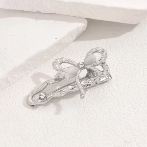 Macro detail of a silver bow hair clip featuring elegant pearls and rhinestones on stone