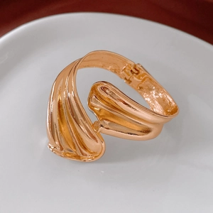 Macro shot of wavy gold open cuff bracelet with a polished metallic texture on white tray