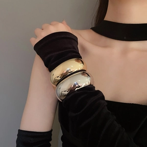 Close-up of polished gold and silver oval wide bracelets on model's wrist with mirror finish