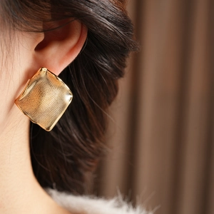 Gros plan d'un mannequin portant de grandes boucles d'oreilles carrées dorées à texture