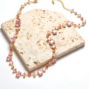 Detailed view of 18K gold plated necklace with pink crystals on beige travertine block