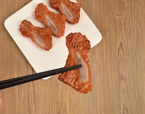 Macro shot of realistic artificial braised pork rib held by black chopsticks on white plate