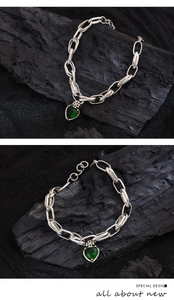 Detail of silver chain bracelet featuring a heart green zircon and cross pendant
