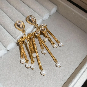 Détail de boucles d'oreilles dorées à pampilles avec cristaux et perles blanches