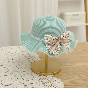 Détail d'un chapeau de paille vert menthe avec nœud floral et bordure en dentelle