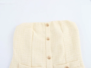 Detail eines beigen Tweed-Schlauchkleides mit Goldknöpfen und gewebten Taschen
