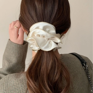 Chouchou élégant en satin blanc avec bord doré sur une coiffure en queue de cheval