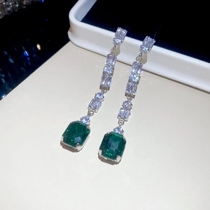 Detailed close-up of silver earrings with green rectangular gems and sparkling zircons
