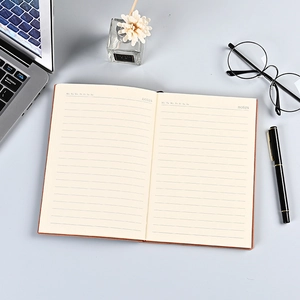 Brown faux leather A5 business notebook with lined pages and stationery on a desk