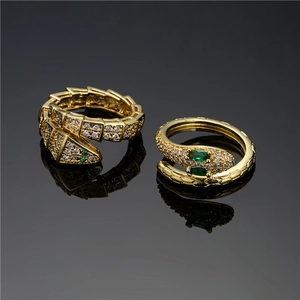 Detail view of gold snake rings with green gemstones and white zircon on black reflective surface