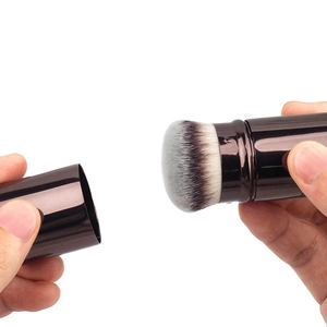 Detail view of a retractable makeup brush with bronze metal casing and dense dual-tone bristles