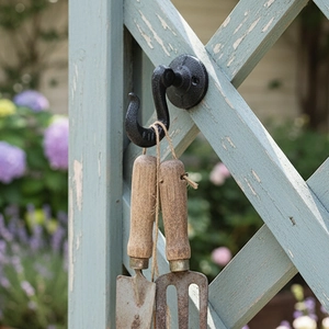 Vintage black cast iron wall hook with rustic gardening tools on blue wood