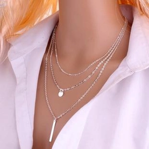 Close-up of layered silver metal necklace featuring small round and bar pendants