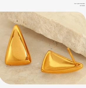 Macro shot of minimalist gold triangle stud earrings on natural textured stone background