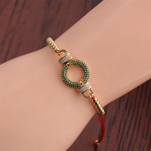 Detail of red braided bracelet featuring gold beads and green zircon encrusted ring
