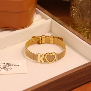 Détail d'un bracelet en maille dorée avec breloque lettre K et pendentif cœur évidé