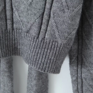Close-up of grey cable knit texture and ribbed hem detail on the backless sweater