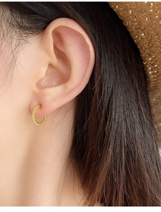 Close-up of a gold-toned C-shaped twisted rope earring worn on a female earlobe