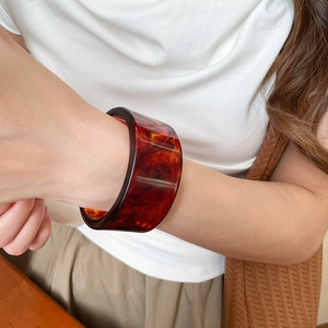 Detail of a wide resin bangle with tortoise shell pattern on a female model wrist
