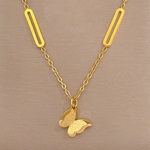 Close-up of a gold butterfly pendant necklace on grey fabric, minimalist titanium steel style
