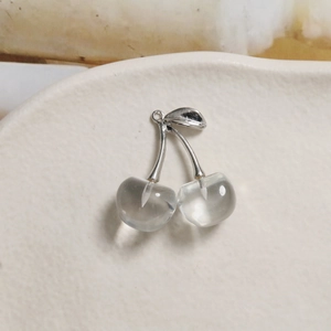 Macro shot of transparent resin cherry pendants with silver metal stems on ceramic surface