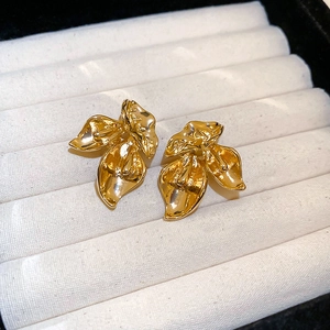 Macro shot of gold floral earrings with polished textured petals on white velvet stand