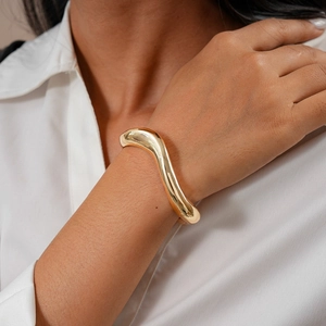 Close-up of a chunky golden wavy cuff bracelet with a polished organic streamline design