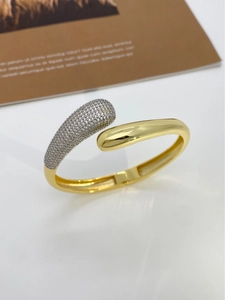 Detail of gold teardrop open bangle featuring pave set zircons and polished finish
