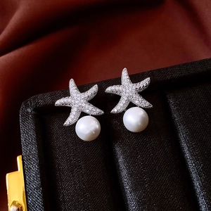 Detailed close-up of starfish pearl earrings with cubic zirconia on black jewelry box