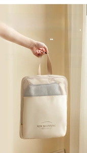 Detail of a beige travel storage bag featuring a wide carrying handle and mesh panels