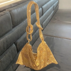 Close-up of golden rhinestone mesh handbag featuring a decorative knot handle detail
