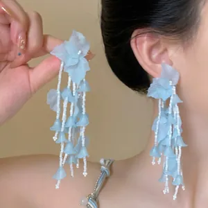 Detail of light blue floral tassel earrings with white beads on a female model