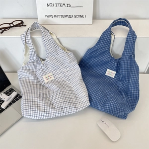 Close-up of blue plaid cotton tote bags with minimalist cloth labels on a white desktop