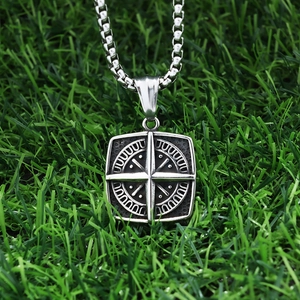 Detailed close-up of square compass pendant on box chain over green grass