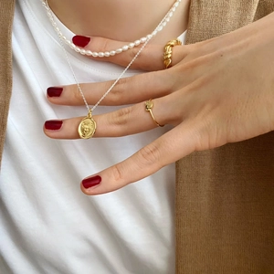 Detailed view of gold smile pendant, pearl necklace and woven rings worn by a model
