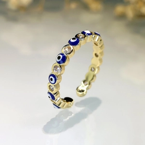 Golden Evil Eye open ring with blue enamel and zircon stones on a white surface