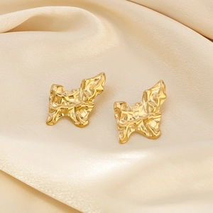 Retro butterfly textured gold metal stud earrings on beige silk fabric background