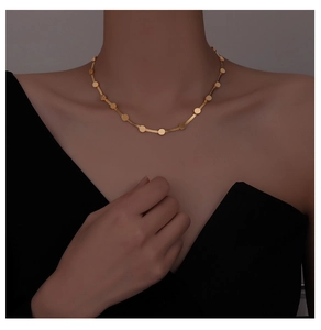 Detail of a gold-plated snake chain necklace with polished round disks on a model