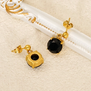 Detail of gold earrings with black round zircon gems on a vintage textured backdrop