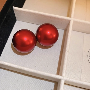 Close-up of polished red round faux pearl earrings resting in a beige jewelry box tray