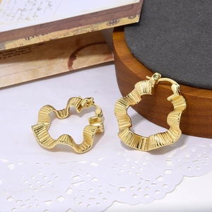 Golden wave-shaped hoop earrings with textured metal finish on minimalist wood background