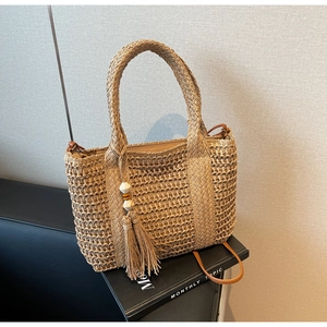 Detail of khaki straw tote bag with braided handles, tassels and wooden beads decor