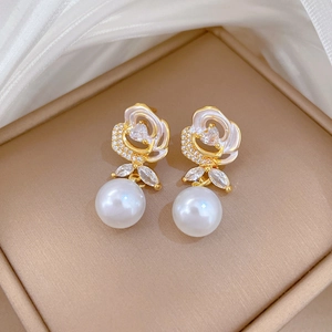 Close-up of golden enamel rose earrings with crystal accents and white pearl droplets