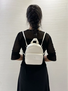 Close-up of mini white leather backpack with flap pocket shown on model against a wall