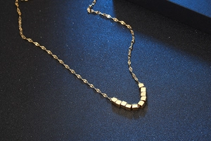 Detail of minimalist gold titanium steel necklace with square beads on textured background