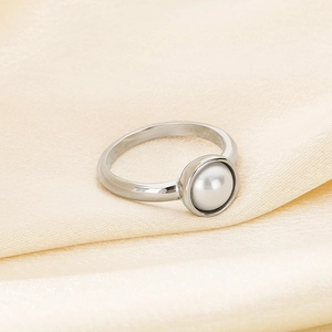 Nahaufnahme eines silbernen Edelstahlrings mit weißer Perle auf weichem Seidenhintergrund