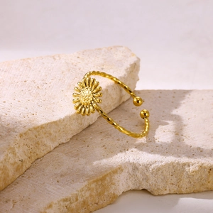 Macro detail of gold daisy ring with twisted band on beige stone background