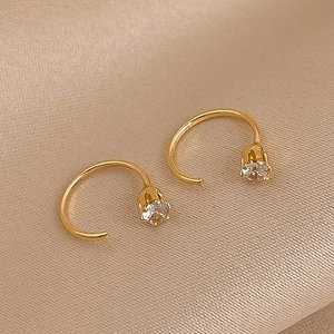 Detail of gold geometric C-shaped earrings with sparkling cubic zirconia on satin
