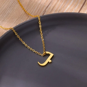 Macro shot of gold Arabic letter B pendant on fine chain over grey ceramic plate